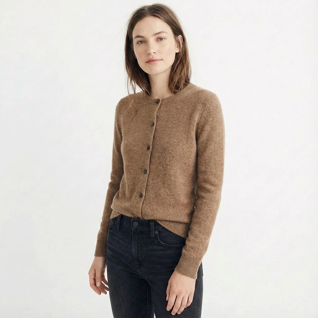 Brunette woman wearing a brown cardigan and dark jeans with a slight smile