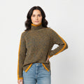 Woman wearing a turtleneck sweater with yellow accents and blue jeans on a white background