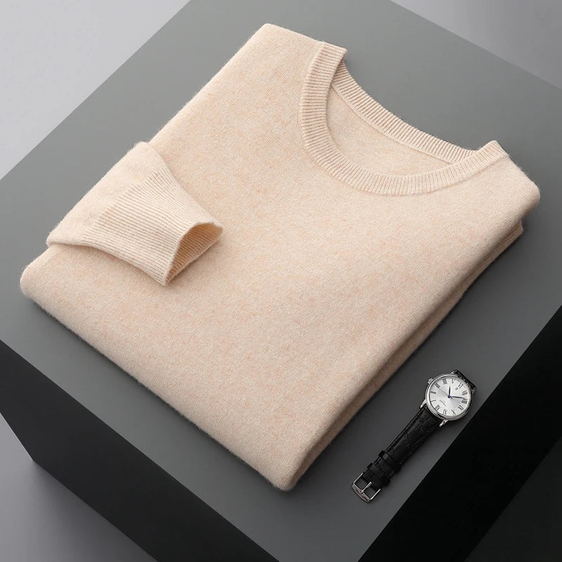 Folded beige brexton men's merino wool sweater on a dark surface with a watch beside it