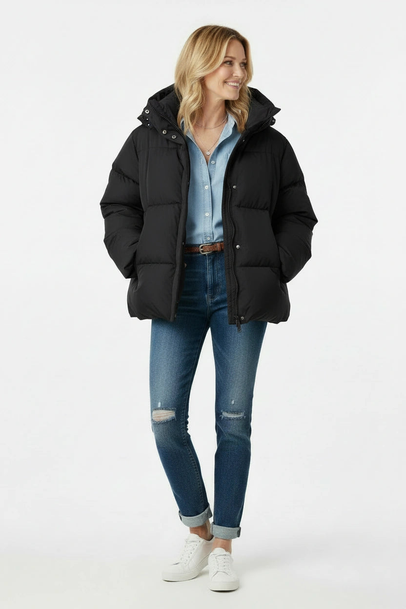 Woman wearing a black puffer jacket, blue jeans, and white sneakers on a white background