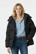 Woman wearing a black puffer jacket over a blue shirt and jeans on a white background